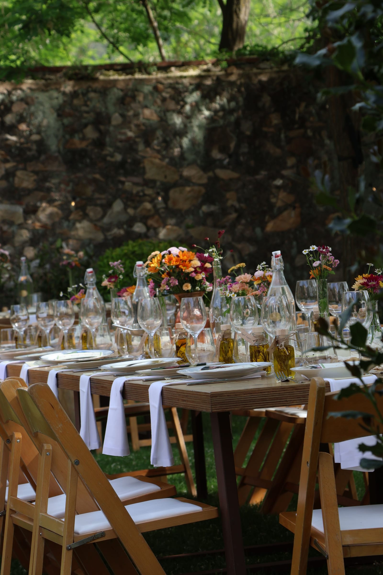 Mesa larga con flores y copas bajo los árboles