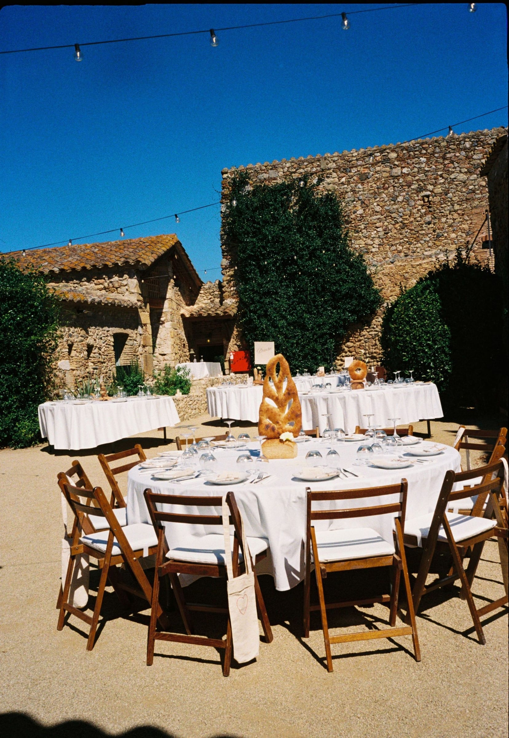 Mesas redondas en un patio soleado junto a una casa de piedra